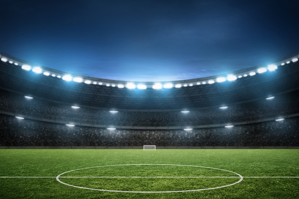 Floodlit football stadium at night with a green pitch