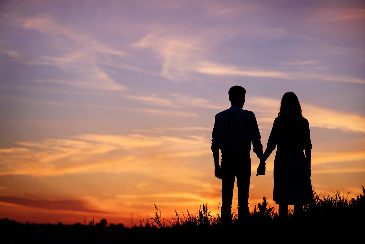 Young couple holding hands silhouetted against a sunset