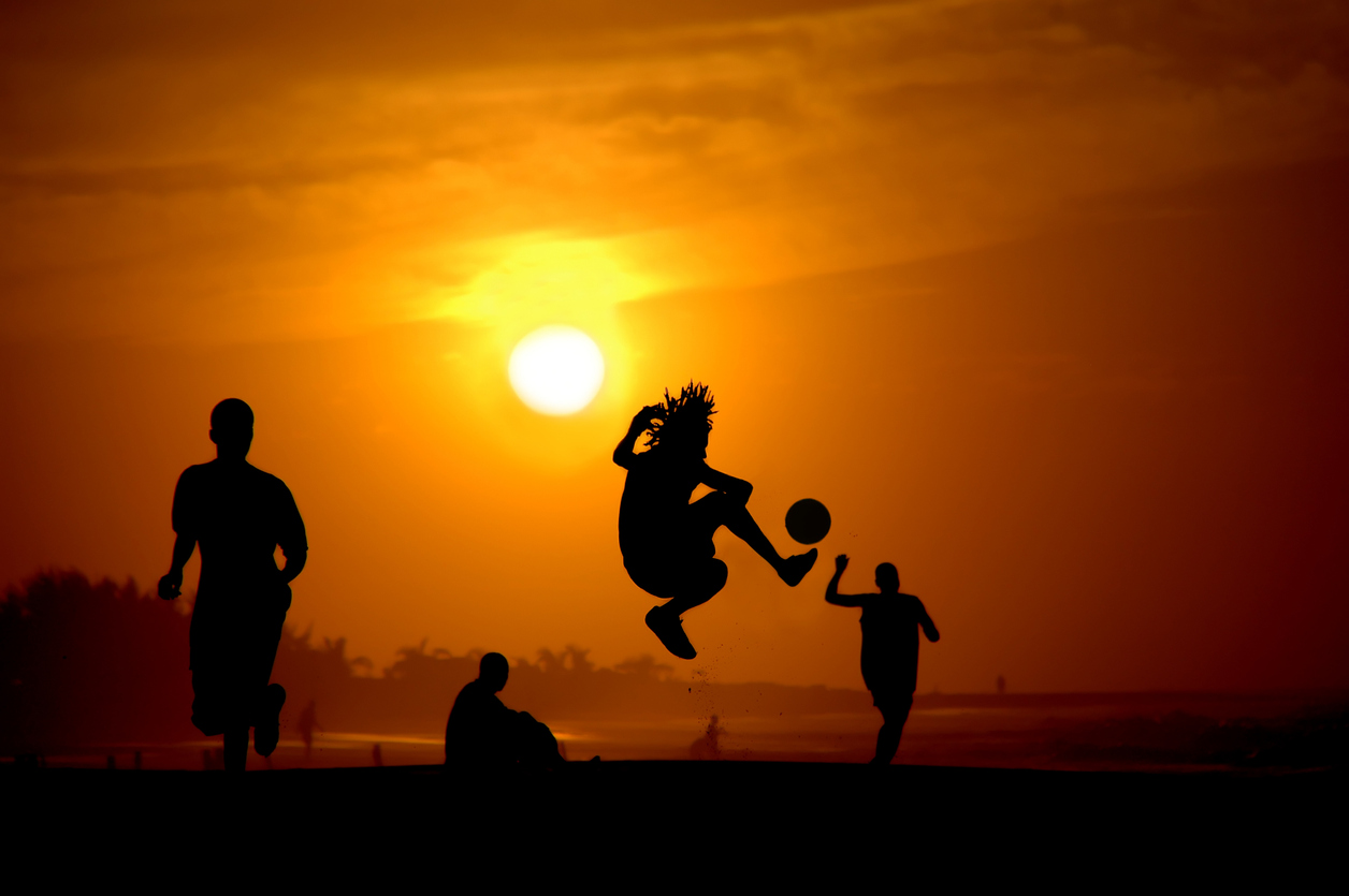 Players silhouetted playing street football at sunset